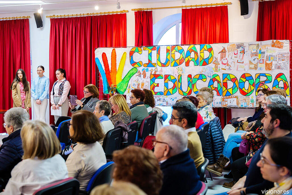 De pie, las presentadoras del acto, ante uno de los grandes paneles conmemorativos - Créditos VISIONAR