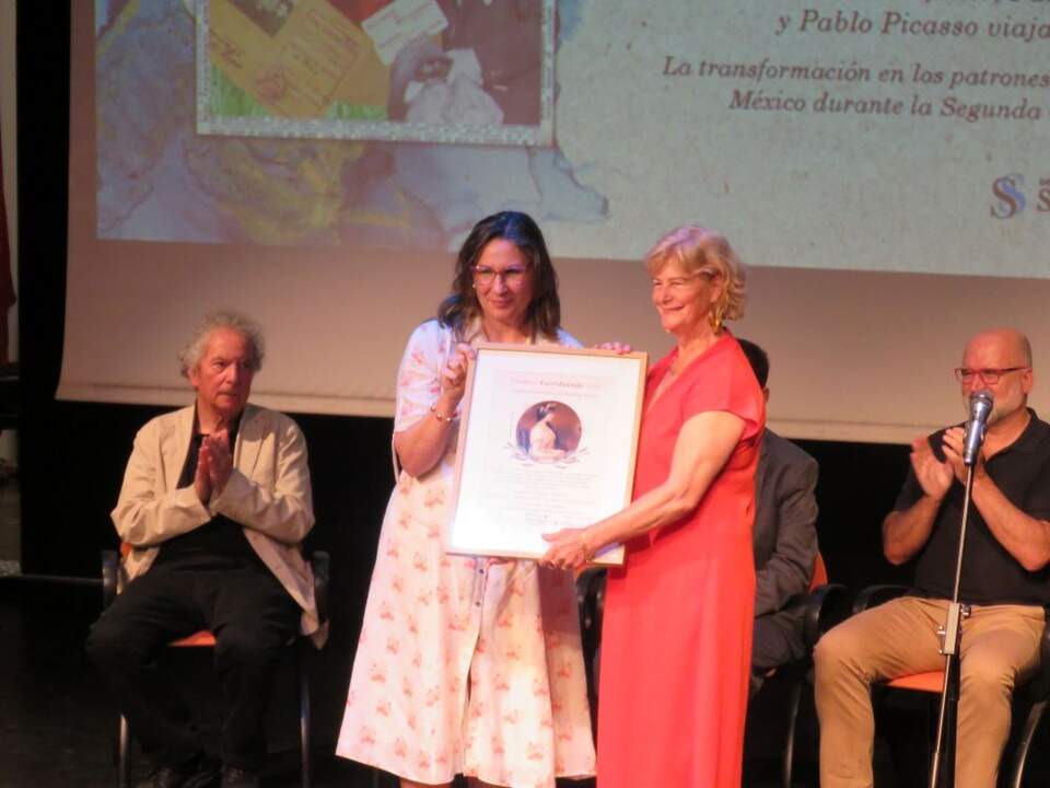 Raquel Delgado López, a la izquierda, entrega a María del Carmen Alberú Gómez, coautora de la obra Nelson Rockefeller, Pancho Pistolas y Pablo Picasso viajan a México. La transformación en los patrones de consumo de arte en México durante la Segunda Guerra Mundial, premio al Mejor libro artístico